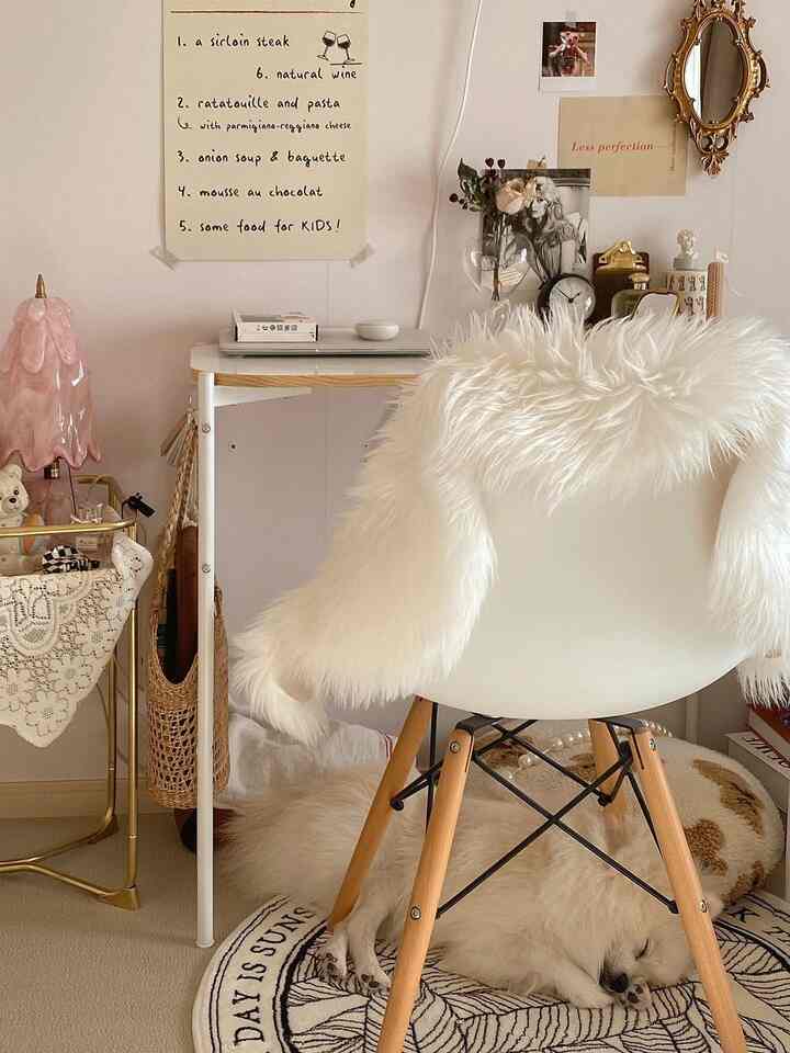 Ivory and natural-toned bedroom space featuring a white armchair, rug, and desk with a cozy white dog resting underneath