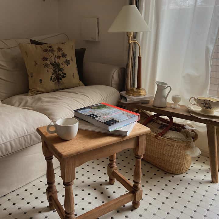 ベージュと木目調の調和が美しい居心地のよいリビング、ソファと木製テーブル、花瓶、カーテンが配置された雰囲気のあるインテリア