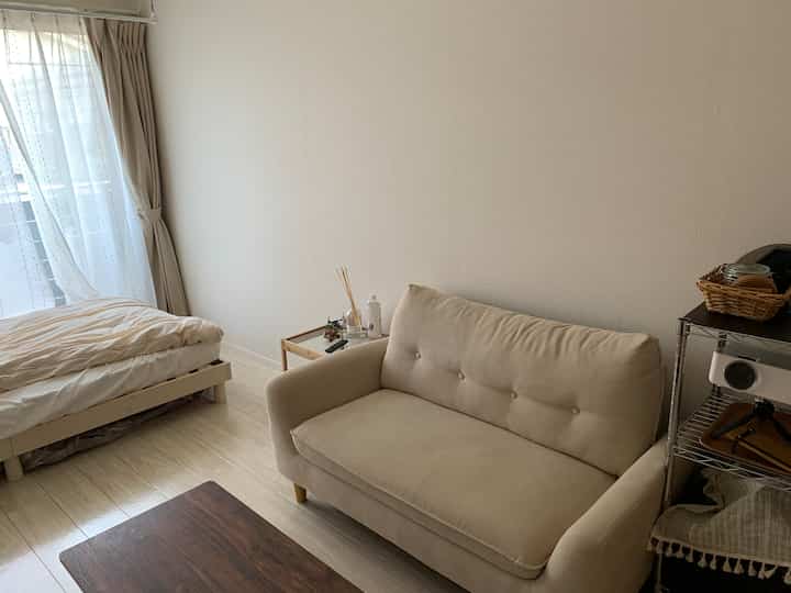 ベージュとナチュラルカラーの落ち着いた寝室、ソファとベッドが配置されたシンプルで清潔感のあるインテリア