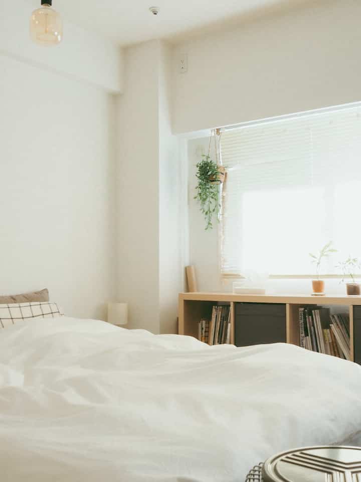 白を基調とした1LDKの寝室、窓辺に棚とブラインドが配置された清潔感のある明るいインテリア