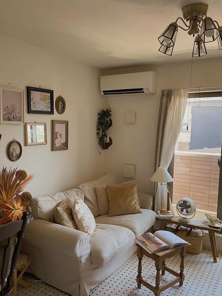 Cozy living room with white and natural tones featuring a white sofa, wooden side tables, and wall posters creating a warm atmosphere