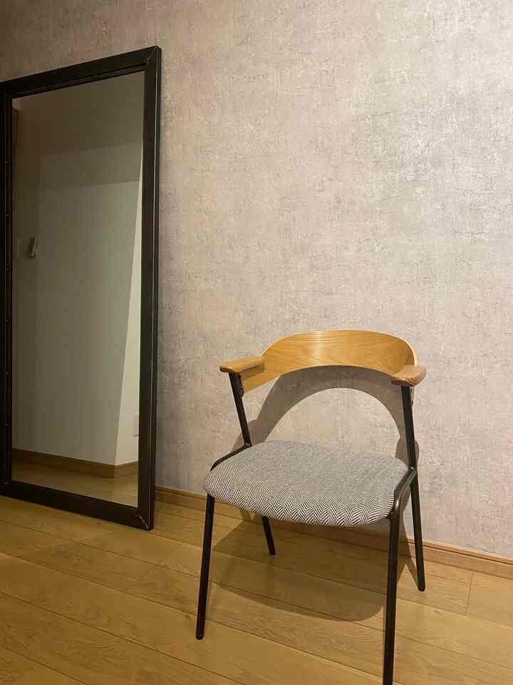 A cozy space with brown wood flooring and gray walls featuring an armchair with wooden armrests and a large standing mirror, natural interior style