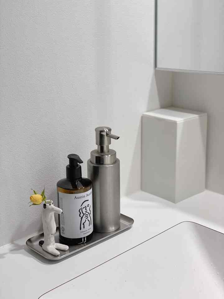Minimal bathroom sink area in white and stainless steel tones featuring hand soap and tray on countertop
