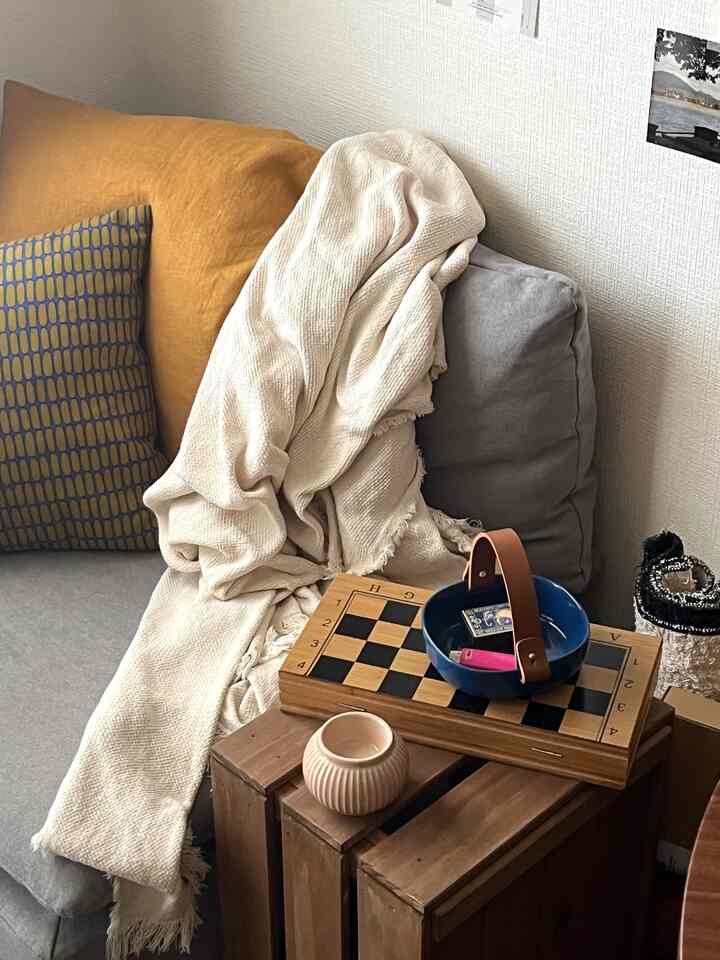 ベージュとグレーのトーンのリビングコーナー、チェスボードと木製の収納箱が置かれた居心地の良い一人暮らしの空間