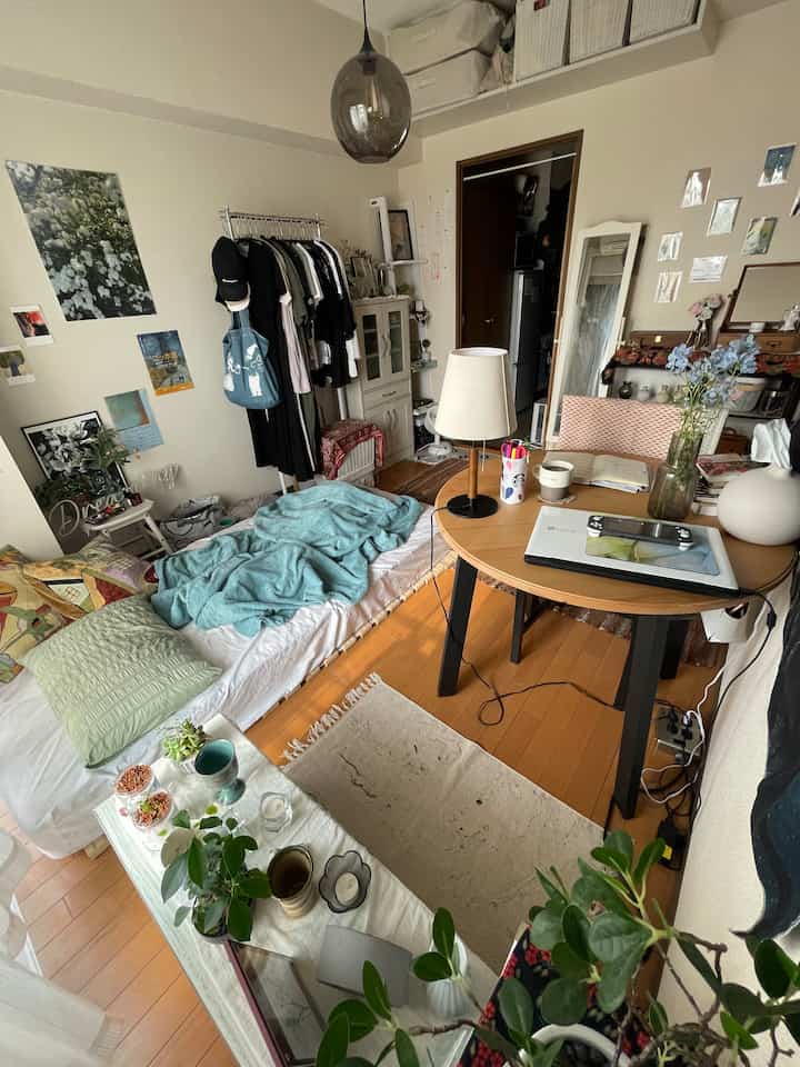 ベージュの壁と木目調の床が調和する狭い一人暮らしのリビング、ベッド兼用のマットレスと丸い机が配置されたナチュラルでモダンな空間