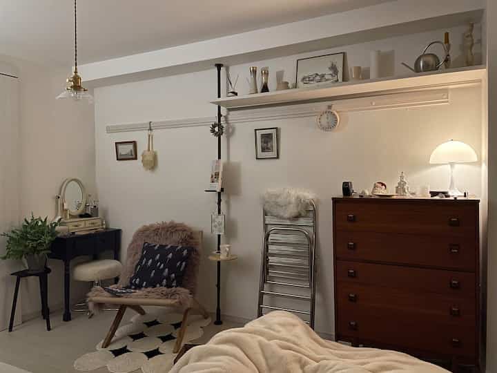 Natural-toned bedroom with white walls and a brown dresser, cozy throw and chair arranged in a warm atmosphere