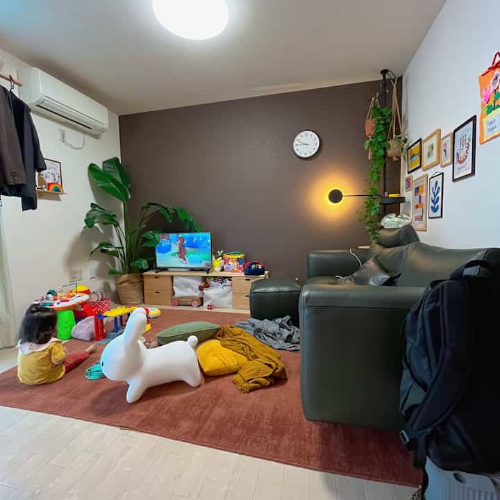 ブラウンのラグとナチュラルカラーの壁が特徴的なリビング、子供の遊び道具が散らかった家族の空間