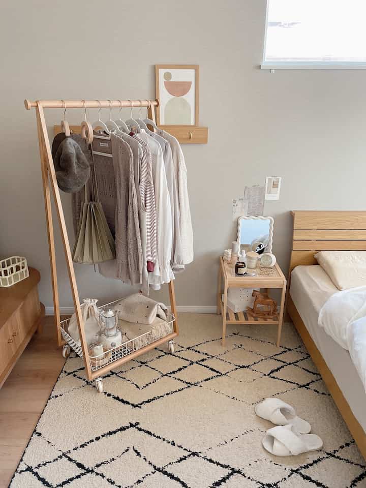 ナチュラルな木目調とホワイトカラーの寝室、木製ハンガーラックとナイトテーブルが配置された居心地の良い空間