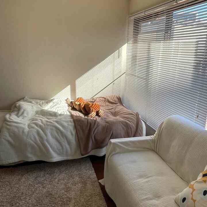 温かみのあるナチュラルトーンの寝室、白いブラインドとソファ、ベッドが配置された雰囲気のあるインテリア