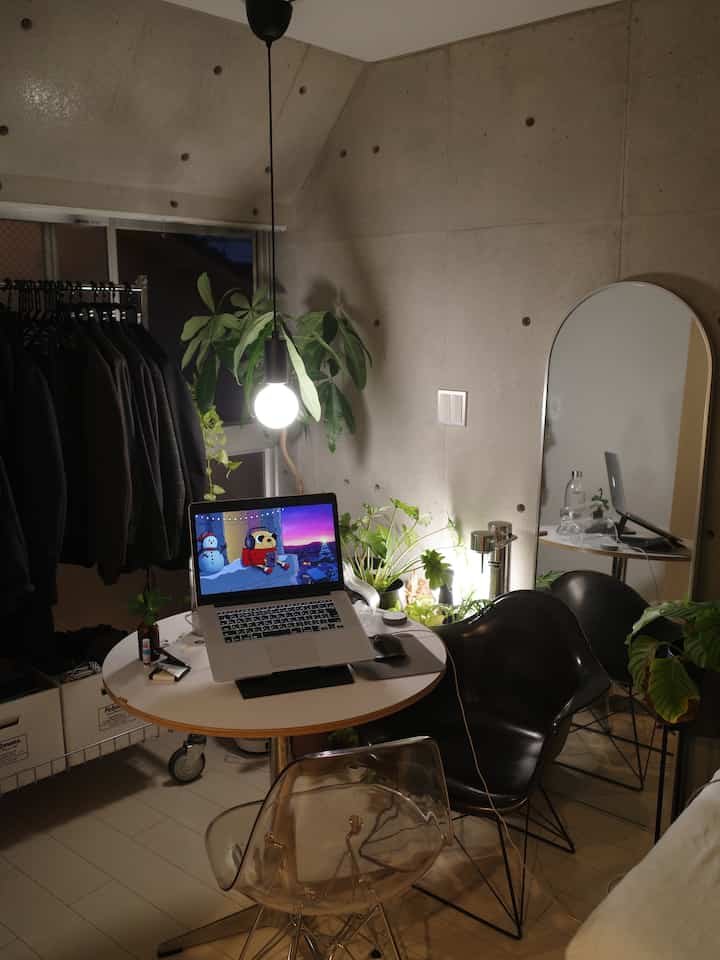 Small studio space with concrete walls featuring a white round dining table, black chairs, and green plants as accents