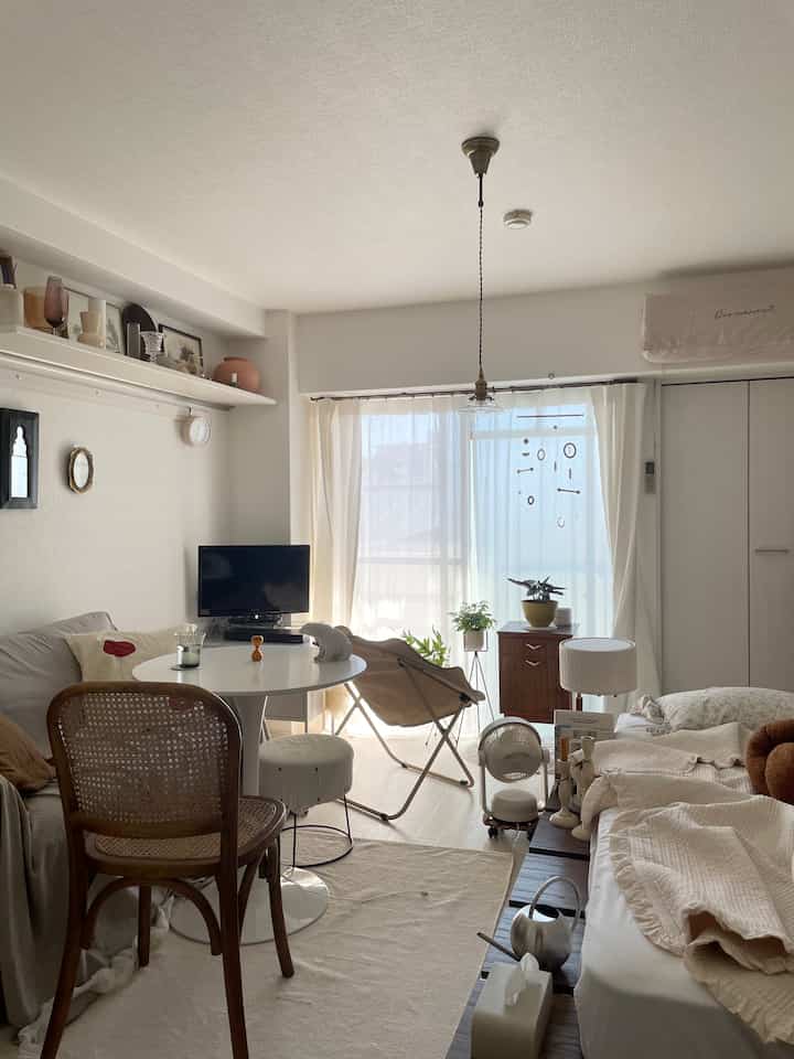 明るくナチュラルな色調のリビング、一人用ベッドと丸いダイニングテーブル、ペンダントライトが配置された雰囲気のあるインテリア