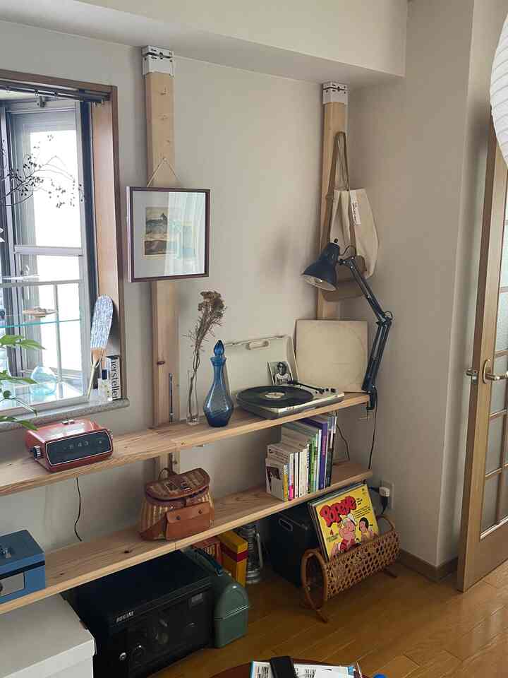 ナチュラルな木目調とレトロな雰囲気の一人暮らしの狭い部屋、ヴィンテージアイテムと本棚が配置された印象的な空間