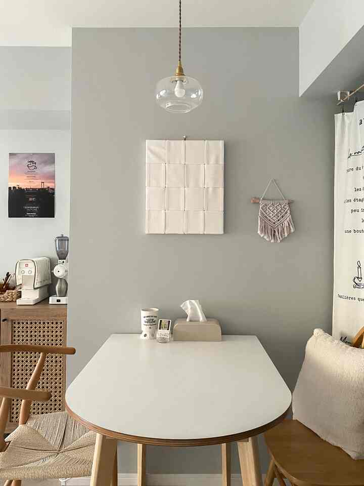 Simple dining room with gray walls and natural wood tones, featuring a white dining table, pendant lighting, and wall decor creating a cozy atmosphere