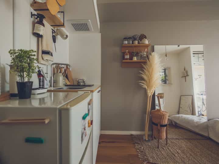 ベージュと木目調が調和した狭いキッチンスペース、壁掛け棚と大型の鏡が配置された自然な雰囲気のインテリア