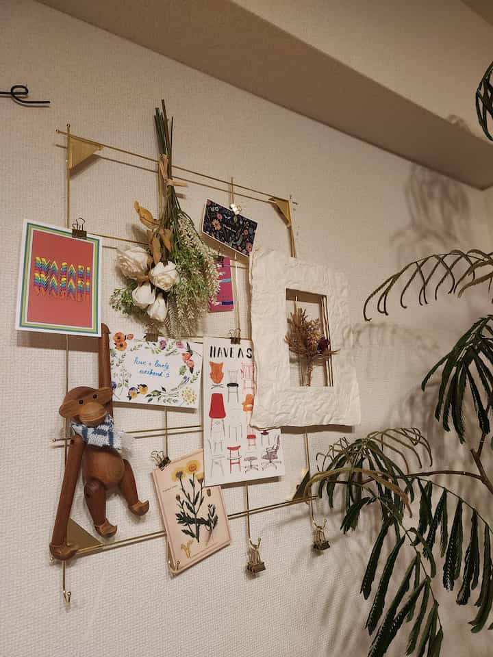 ゴールドのスチールフレームに複数のポスターと木製の装飾品が配置されたナチュラルな雰囲気の壁面インテリア