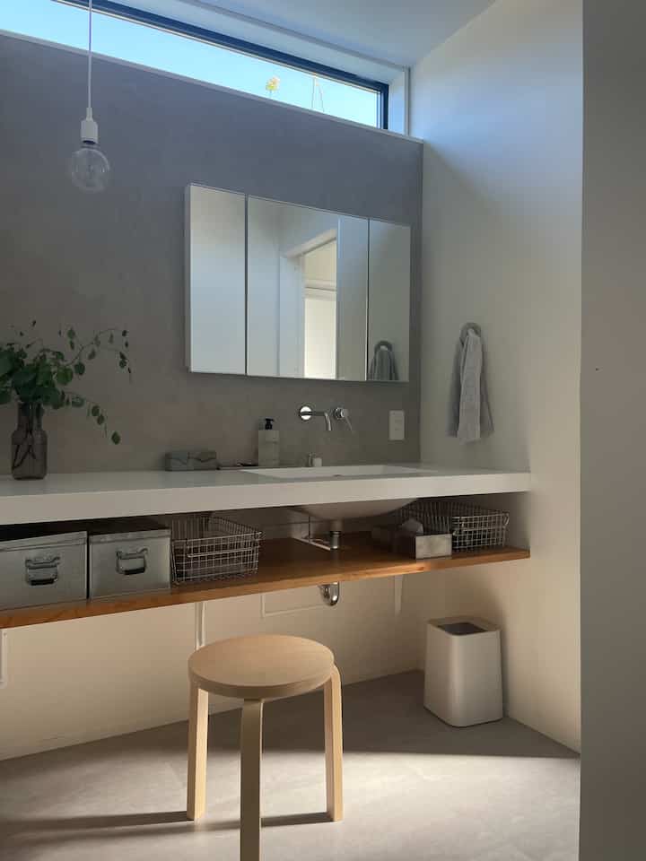 白とナチュラルカラーのバスルーム、スツールと収納棚が配置されたシンプルで明るい印象的な空間