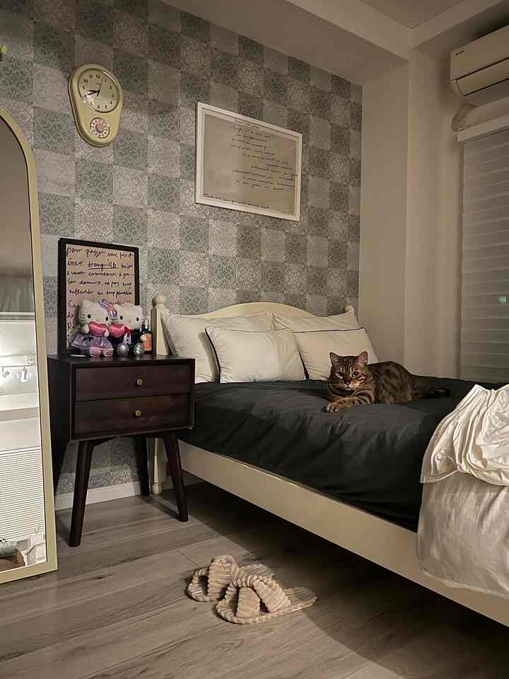 木目調の床と黒い寝具がある猫と暮らす寝室、ヴィンテージの時計と柄壁紙が印象的な空間