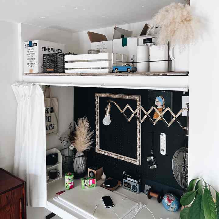 白い壁と机、黒いペグボードが配置されたワークスペースで、ヴィンテージの小物と壁掛けランプが印象的な落ち着いた雰囲気のインテリア