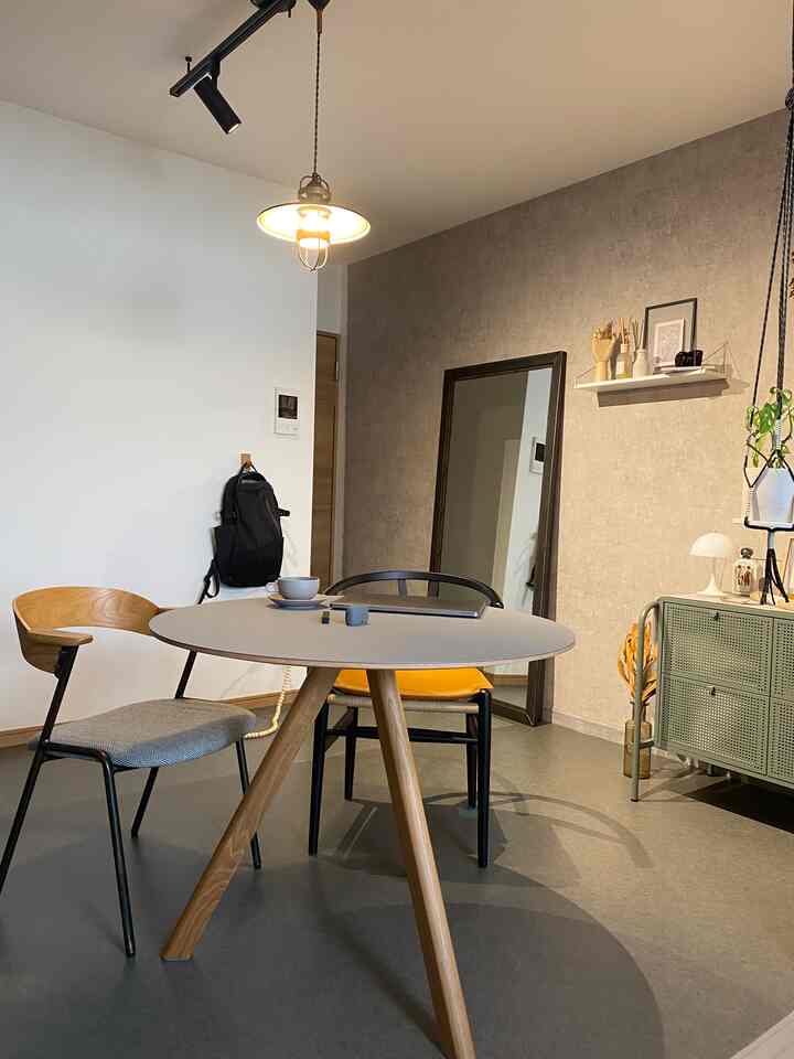 グレーと木目調のモダンなリビングルーム、ラウンドダイニングテーブルとアームチェア、壁掛けミラーとフロアランプが配置された印象的な空間