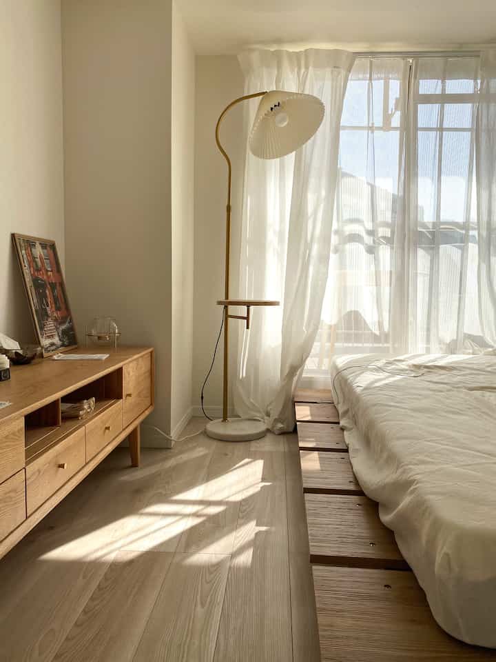 ナチュラルな木目調と白を基調とした寝室、低めのベッドフレームとフロアランプが配置された落ち着いたインテリア