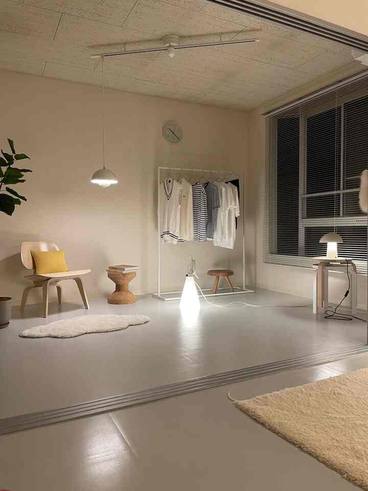 Simple studio apartment in beige and white tones, featuring an armchair, clothes rack, and floor lamp with natural modern interior