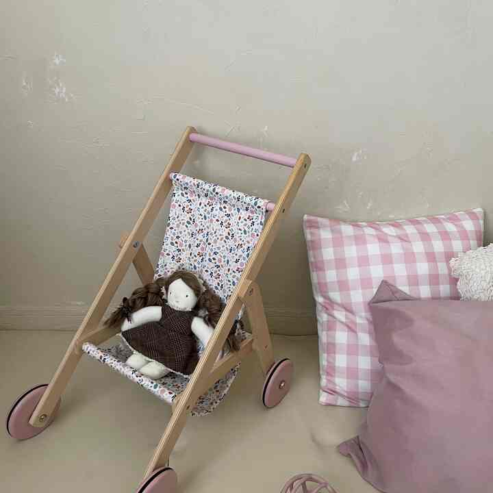 柔らかいナチュラルな色調の子供部屋、木製の人形用バギーとピンクのクッションが配置された温かみのある空間