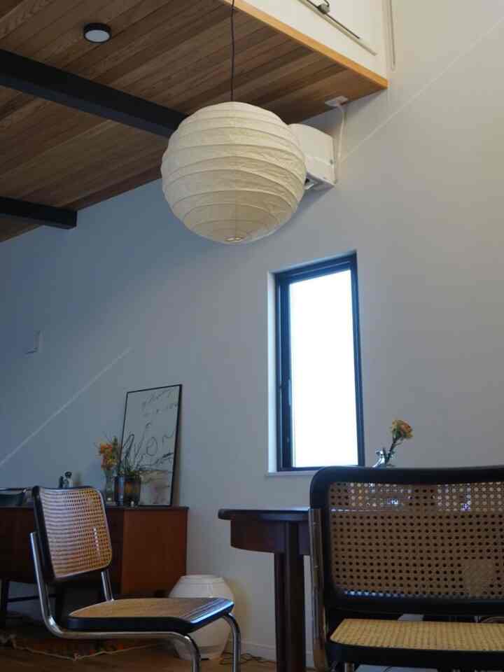 Natural modern dining room with white walls and wood tone ceiling, featuring rattan chairs and a round paper pendant light
