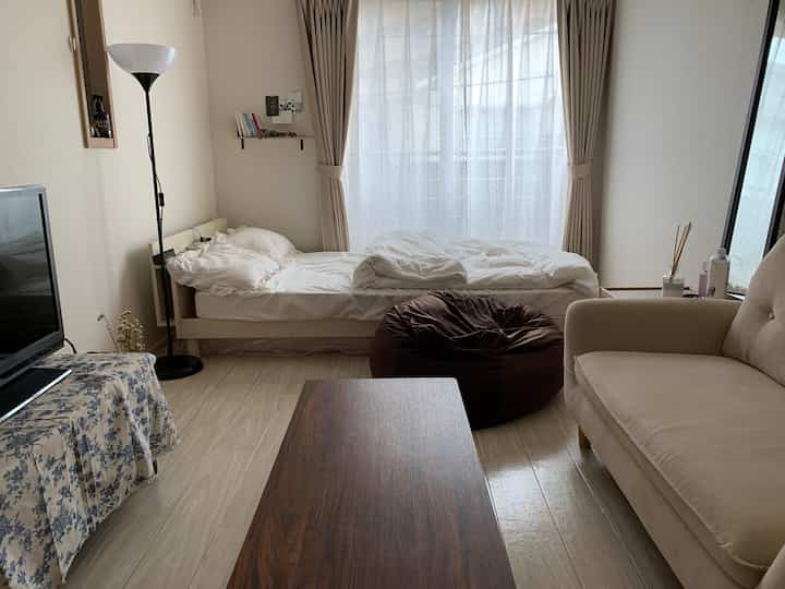 A white and brown toned bedroom featuring a bed, sofa, and bean bag in a cozy compact room