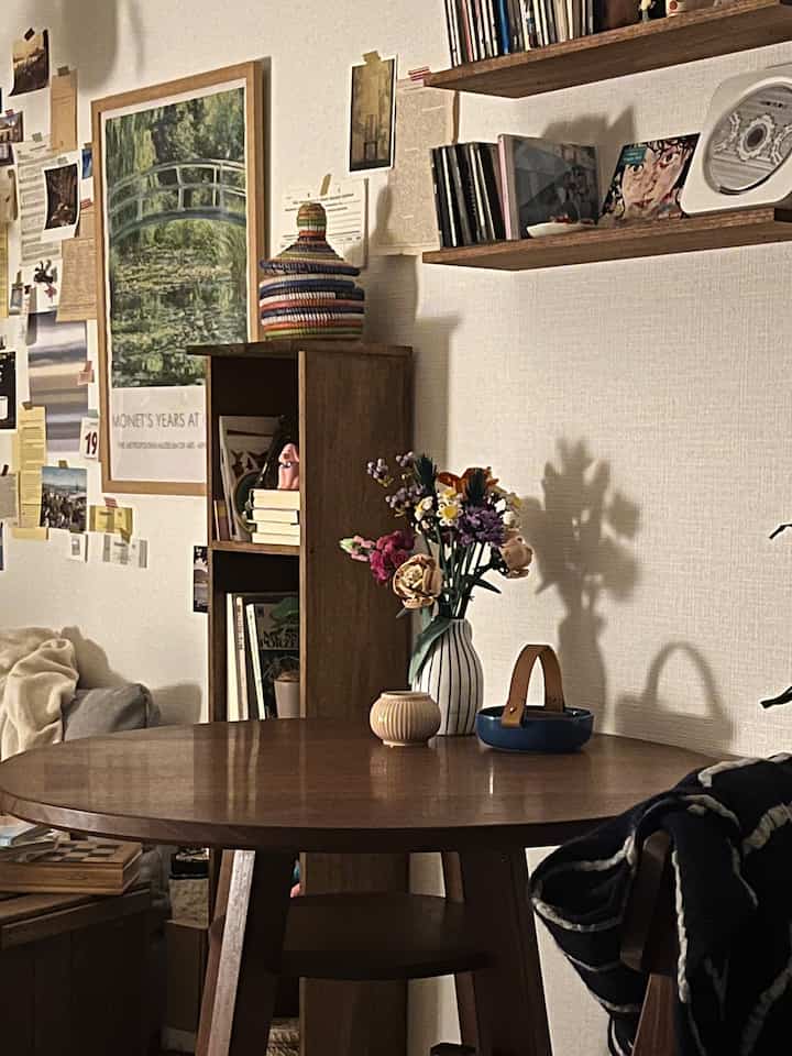 ナチュラルなブラウンとホワイトトーンのワンルームリビング、木製テーブルに花瓶と壁アートが配置された落ち着いた空間