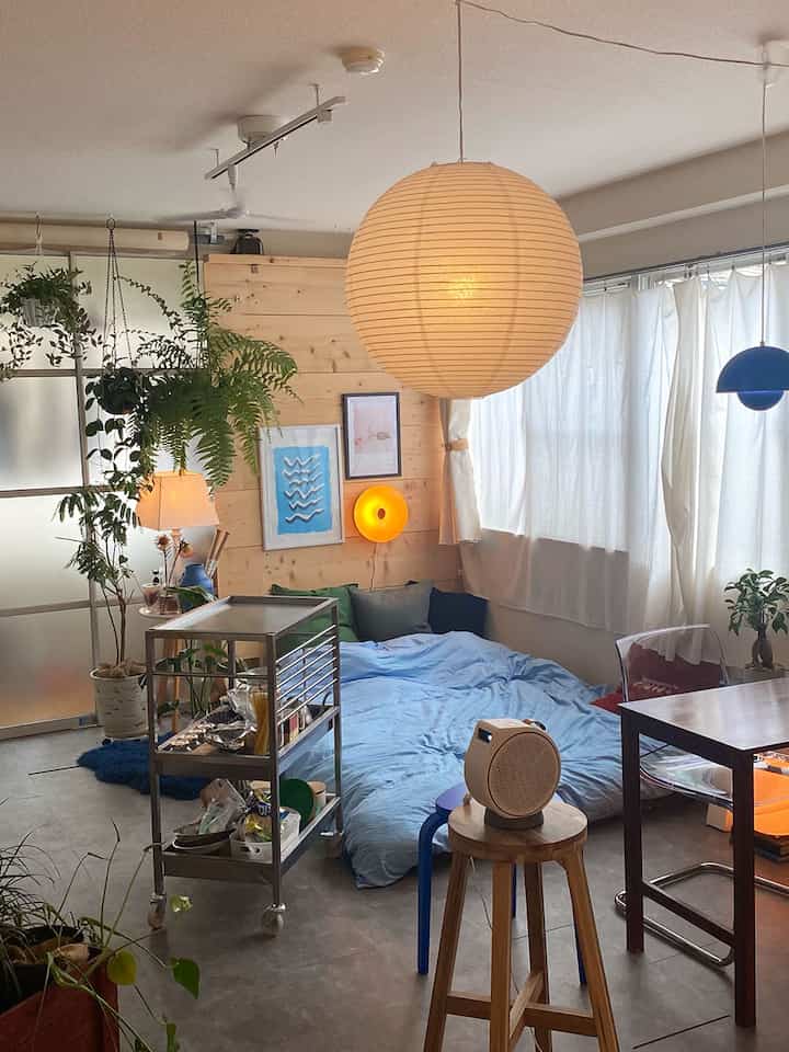 オレンジ色の照明が柔らかく照らすワンルーム、ナチュラルな木の壁と多くの植物が配置された落ち着いた空間