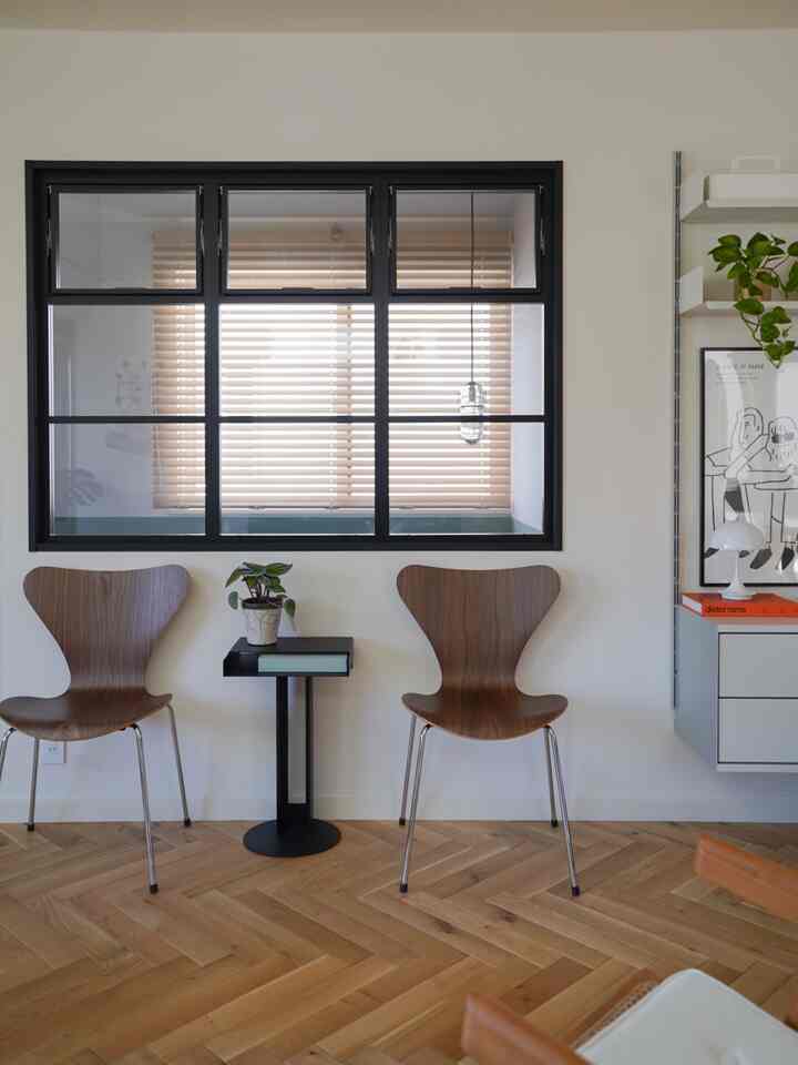 白い壁と黒い枠の窓、ウォールナットチェアと黒いサイドテーブルが配置されたナチュラルモダンなインテリア