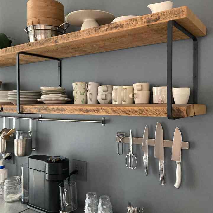 グレーの壁と木目調の棚があるキッチン、さまざまなカップと包丁が整然と配置された印象的な空間