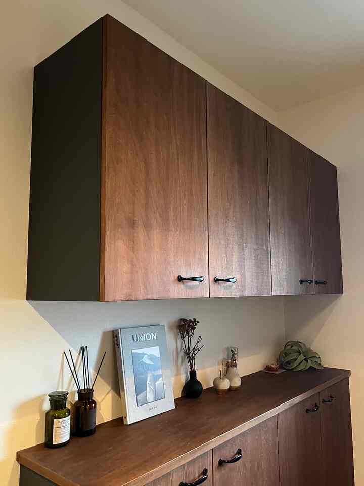 ナチュラルな木目調の玄関、上下に配置された木製クローゼットと中央に花瓶や雑誌が飾られた印象的な空間