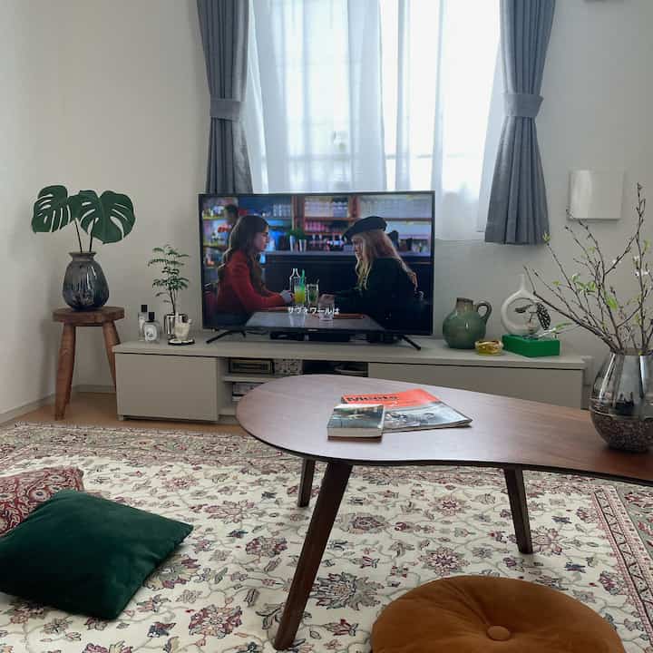 ナチュラルな色調のリビング、中央にテレビ台とラグ、低い木製テーブルとクッションが配置された落ち着いた雰囲気のインテリア