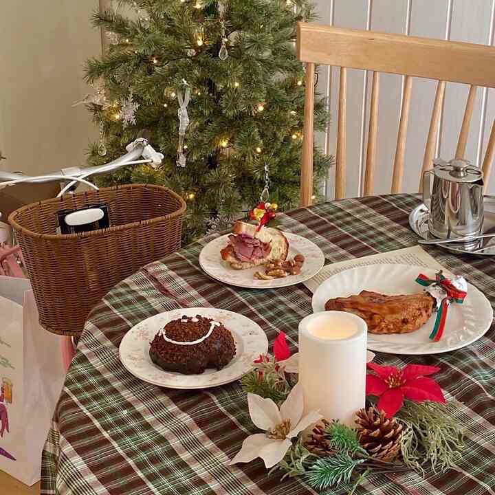 緑のクリスマスツリーを背景に、ブラウンのチェック柄テーブルクロスが敷かれたダイニングルーム。キャンドルと料理が置かれた温かみのあるホームパーティー空間