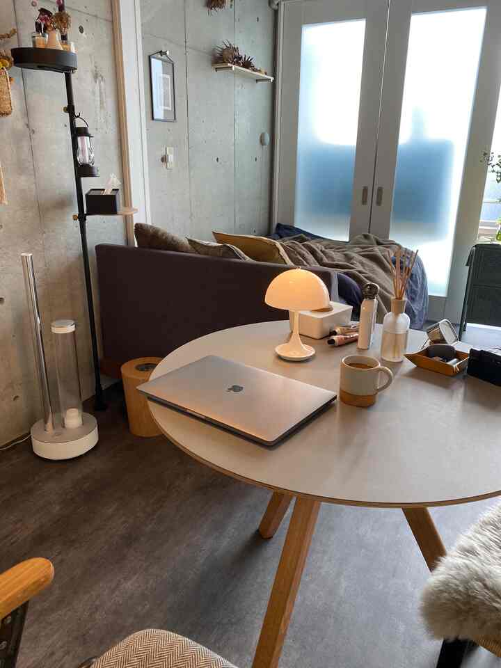 モダンな色調のリビングホームオフィス空間、円形テーブルとソファ、テーブルランプ、作業用ノートパソコンが配置された居心地の良いインテリア