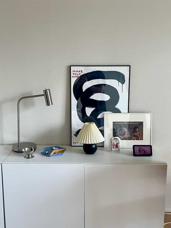 白い収納キャビネットが壁の前に置かれ、モダンな照明と額縁が上に配置された清潔感のある韓国インテリア