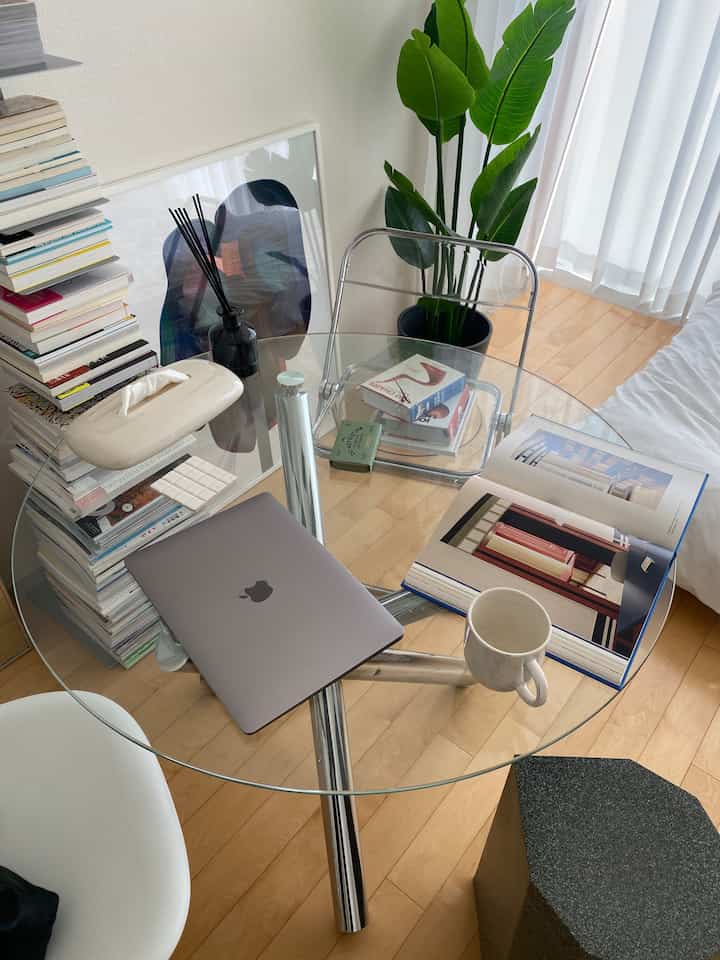 ナチュラルな色調の6畳部屋、丸いガラステーブルにノートパソコンや本、マグカップが置かれたホームオフィスの雰囲気のあるインテリア