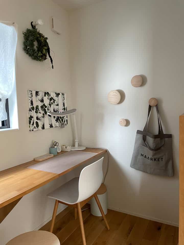 白と木目調の書斎空間、シンプルなデスクと学習ランプ、壁にウッドフックが配置された学習コーナー