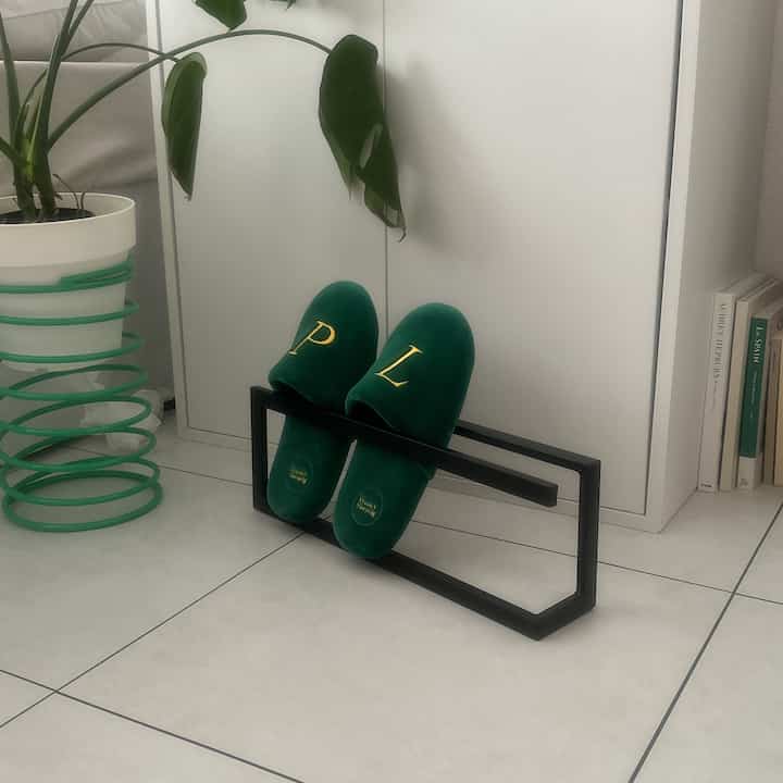 白いタイル床とシンプルな靴収納前に緑色の室内スリッパが置かれた落ち着いた玄関スペース