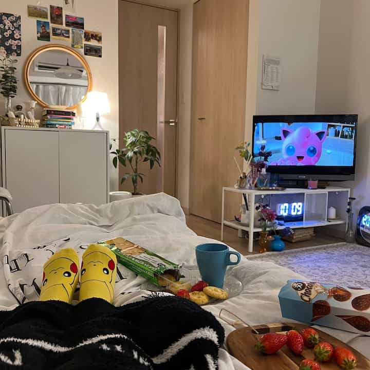 白と木目調の寝室、テレビ台と植物が配置された居心地の良い空間