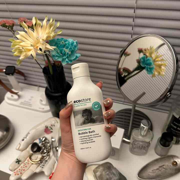 ホワイトとライトグレーの色調のバスルームパウダールーム、花瓶と丸い鏡、エコストアのバブルバス製品が配置された空間