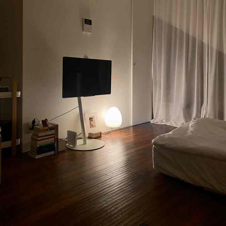 Cozy nighttime bedroom with brown wood flooring, white bedding, lace curtains, and warm indirect lighting