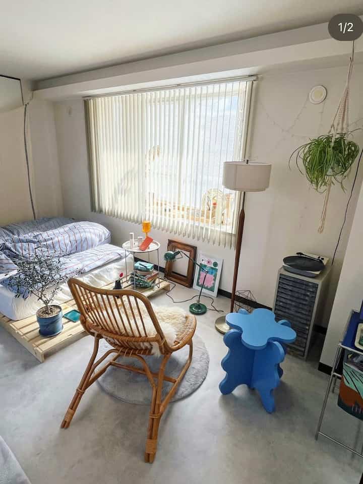 白を基調としたワンルーム、ラタンのアームチェアと青いサイドテーブルが配置された自然でモダンな雰囲気のインテリア