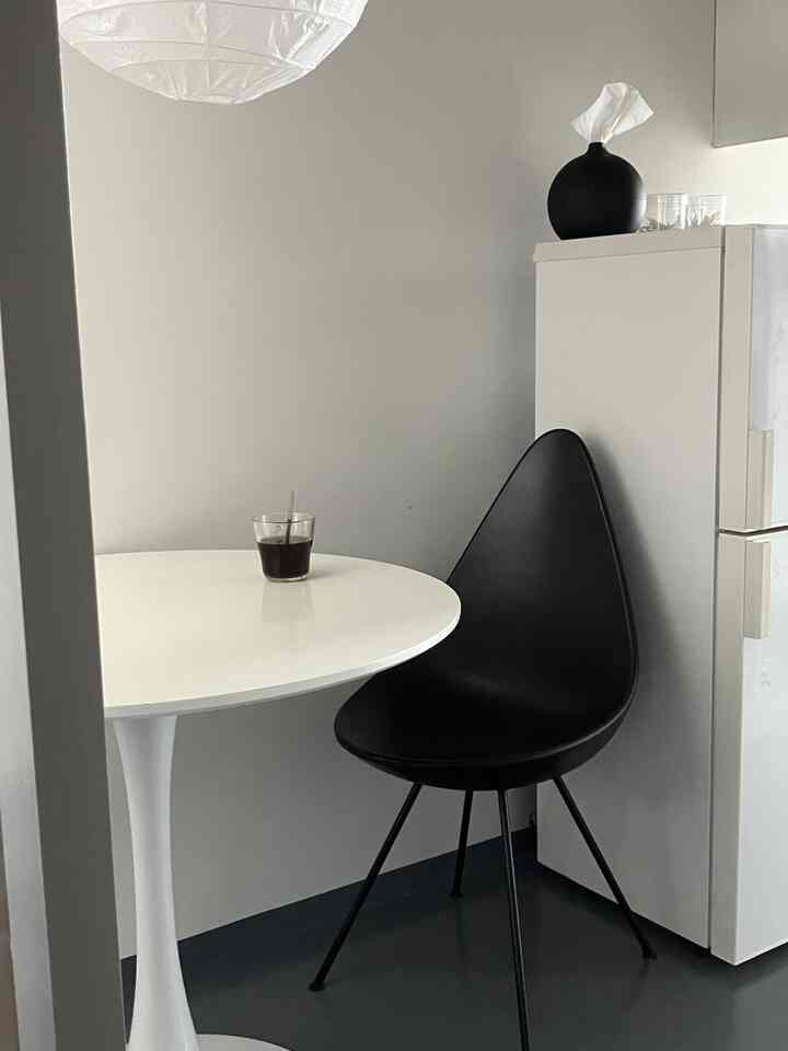 モノトーンの小さなキッチンスペース、白い丸テーブルと黒いダイニングチェアが配置された清潔感のある空間