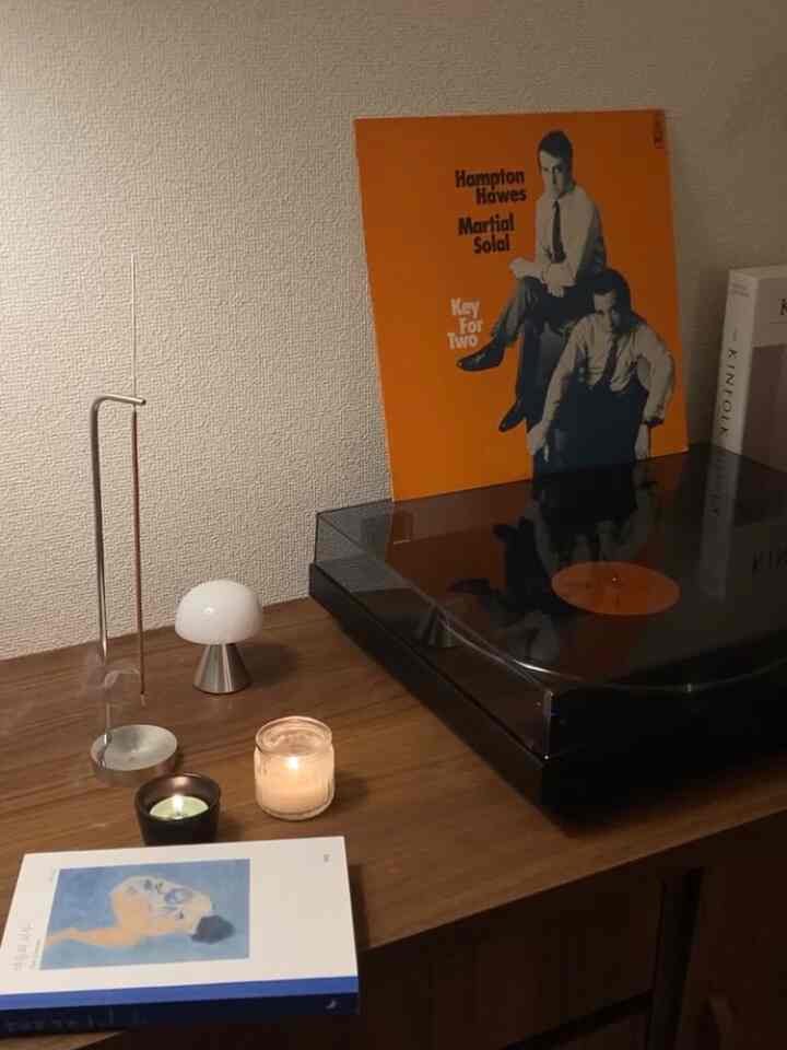 A cozy living room desk with wood tones and black accents featuring a retro Sony record player, books, and lit candles.