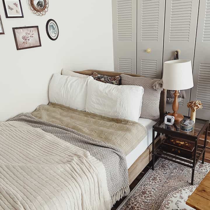 ナチュラルな色調の寝室、ベージュと白の寝具と木目調のナイトテーブルとテーブルランプが配置された雰囲気のあるインテリア