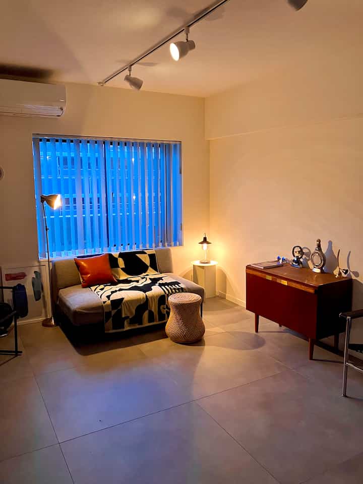 暖かいベージュとブラウンの色調のリビング、スリムなソファとブルーのアルミ製バーチカルブラインドが調和したミッドセンチュリーモダンのインテリア