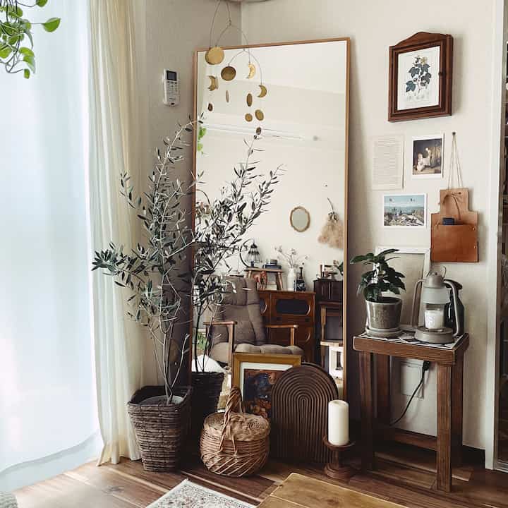 Natural wood-toned living room featuring a large mirror, plants, brass moon mobile, and candle in a cozy setting