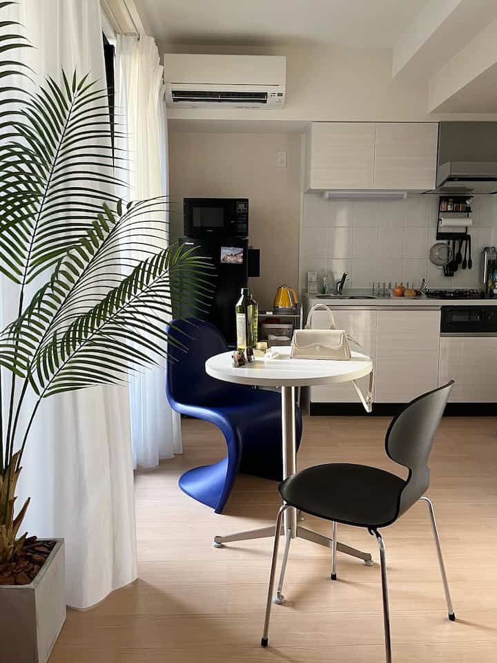 Natural modern kitchen and dining area in white and navy tones featuring a small round table, two chairs, and indoor plant with a clean, simple atmosphere